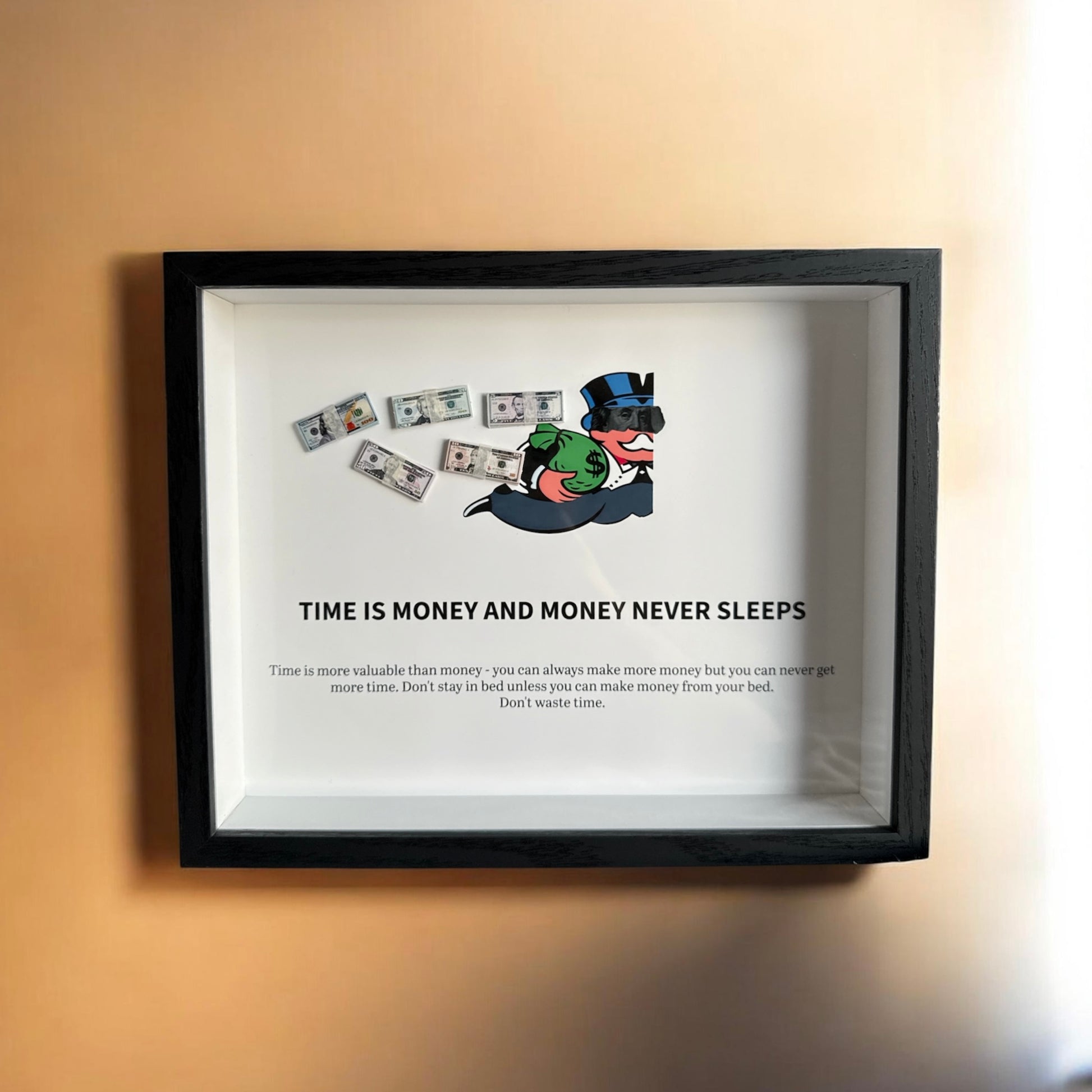 Handmade money shadow box with scattered prop bills and a top-hat tycoon character